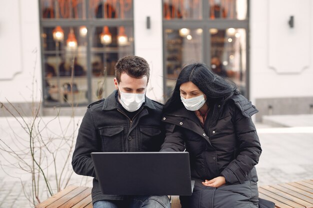 Leute, die eine Schutzmaske tragen, die in einer Stadt mit einem Laptop sitzt