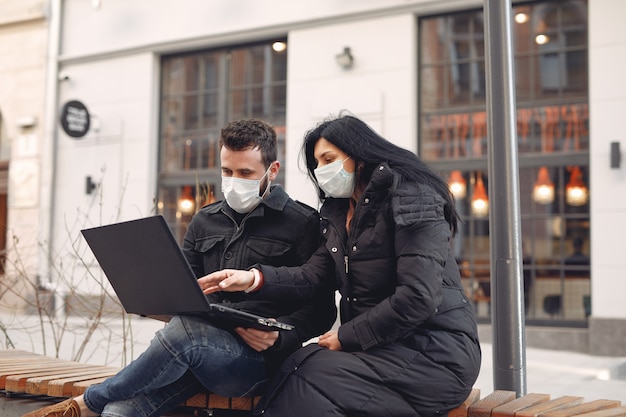 Leute, die eine Schutzmaske tragen, die in einer Stadt mit einem Laptop sitzt