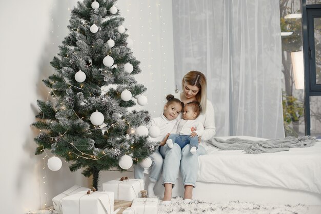 Leute, die sich auf Weihnachten vorbereiten. Mutter spielt mit ihren Töchtern. Die Familie ruht sich in einem festlichen Raum aus. Kind in einem Pullover Pullover.