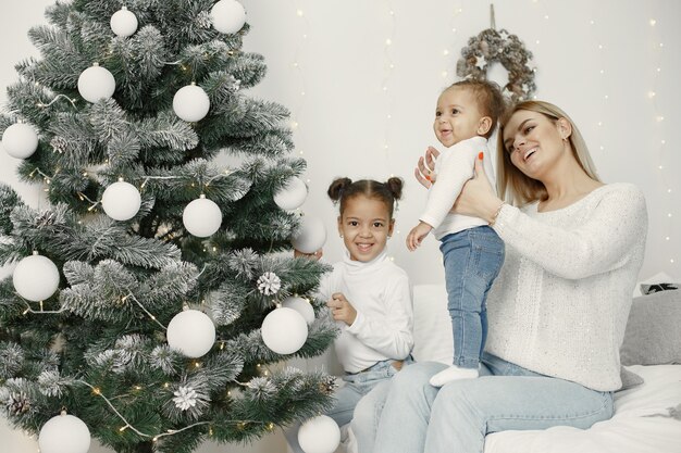 Leute, die sich auf Weihnachten vorbereiten. Mutter spielt mit ihren Töchtern. Die Familie ruht sich in einem festlichen Raum aus. Kind in einem Pullover Pullover.