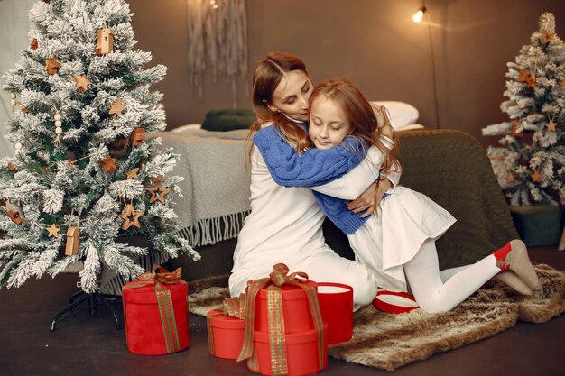 Leute, die sich auf Weihnachten vorbereiten. Mutter spielt mit ihrer Tochter. Die Familie ruht sich in einem festlichen Raum aus. Kind in einem blauen Pullover.