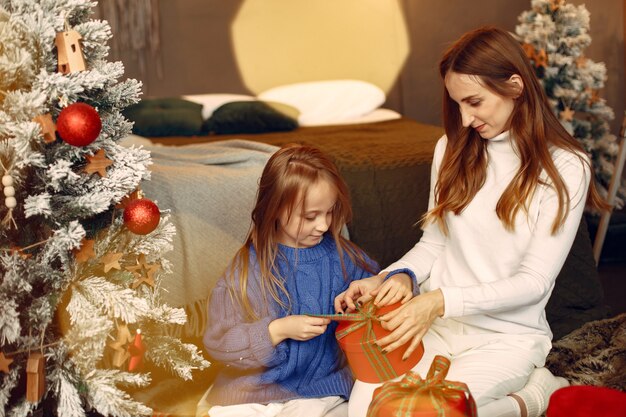 Leute, die sich auf Weihnachten vorbereiten. Mutter spielt mit ihrer Tochter. Die Familie ruht sich in einem festlichen Raum aus. Kind in einem blauen Pullover.