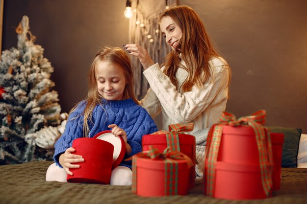 Leute, die sich auf Weihnachten vorbereiten. Mutter spielt mit ihrer Tochter. Die Familie ruht sich in einem festlichen Raum aus. Kind in einem blauen Pullover.