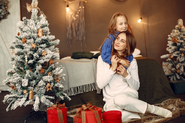 Leute, die sich auf Weihnachten vorbereiten. Mutter spielt mit ihrer Tochter. Die Familie ruht sich in einem festlichen Raum aus. Kind in einem blauen Pullover.