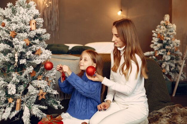 Leute, die sich auf Weihnachten vorbereiten. Mutter spielt mit ihrer Tochter. Die Familie ruht sich in einem festlichen Raum aus. Kind in einem blauen Pullover.