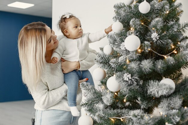 Leute, die sich auf Weihnachten vorbereiten. Mutter spielt mit ihrer Tochter. Die Familie ruht sich in einem festlichen Raum aus. Kind in einem Pullover Pullover.