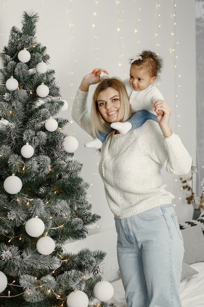 Leute, die sich auf Weihnachten vorbereiten. Mutter spielt mit ihrer Tochter. Die Familie ruht sich in einem festlichen Raum aus. Kind in einem Pullover Pullover.