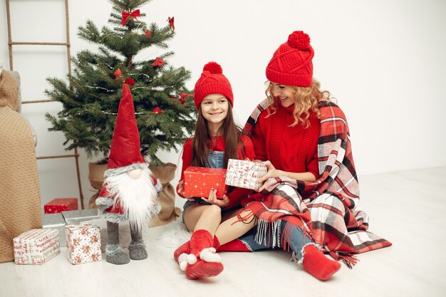 Leute, die sich auf Weihnachten vorbereiten. Mutter spielt mit ihrer Tochter. Die Familie ruht sich in einem festlichen Raum aus. Kind in einem roten Pullover.