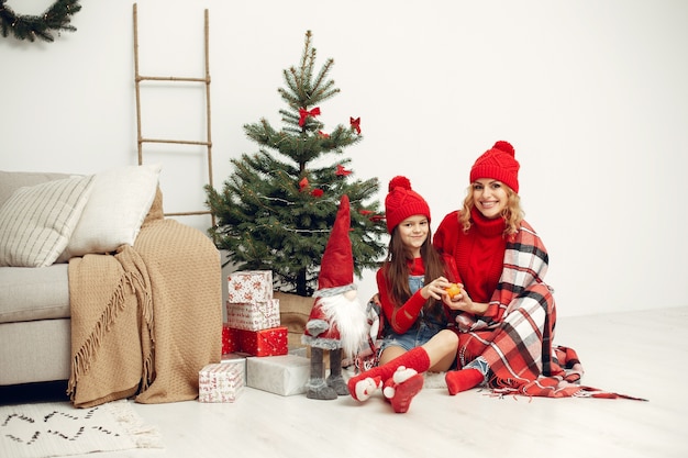 Leute, die sich auf Weihnachten vorbereiten. Mutter spielt mit ihrer Tochter. Die Familie ruht sich in einem festlichen Raum aus. Kind in einem roten Pullover.