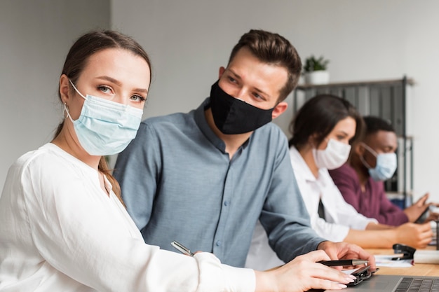 Leute im Büro, die während der Pandemie mit Masken zusammenarbeiten