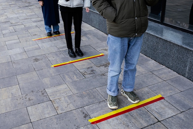 Leute in der Schlange, die hinter dem sozialen Distanzstreifen warten