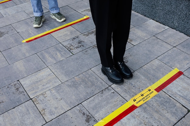 Leute in der Schlange, die hinter dem sozialen Distanzstreifen warten