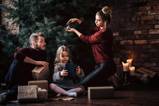 Liebe, Familie, Weihnachtszeit. Attraktive Familie schmückt den Weihnachtsbaum, umgeben von Geschenken zu Hause.