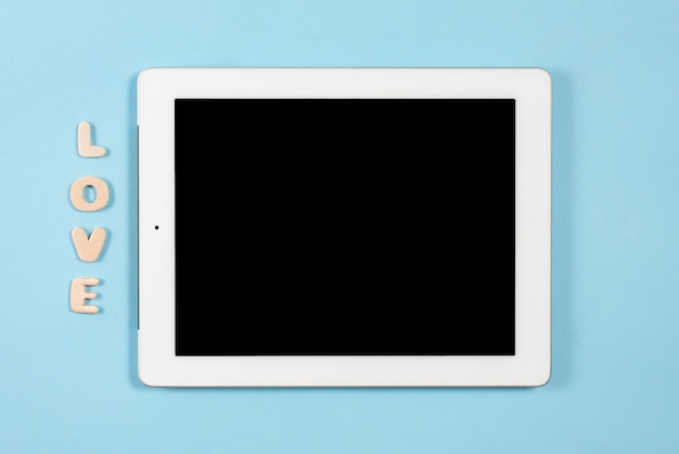 Lieben Sie hölzernen Text nahe der digitalen Tablette mit schwarzer Bildschirmanzeige auf blauem Hintergrund