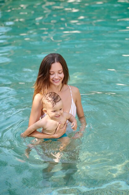Liebendes Wasser. Junge hübsche Frau in einem Swimmingpool mit ihrem kleinen Jungen