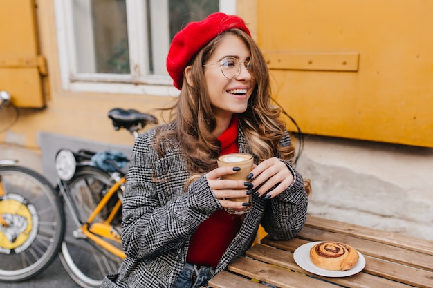 Kostenloses Foto liebenswertes mädchen mit schwarzer maniküre, die im straßencafé mit lächeln kühlt