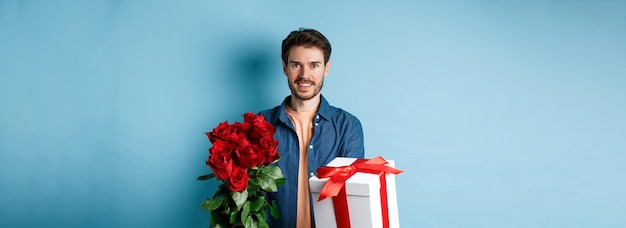 Liebes- und valentinstagkonzept charmanter junger mann, der freundin st geschenk und strauß rosen gibt