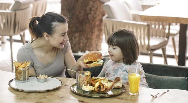 Liebevolle Familie. Mutter mit niedlicher Tochter, die Fastfood in einem Café-, Familien- und Ernährungskonzept isst