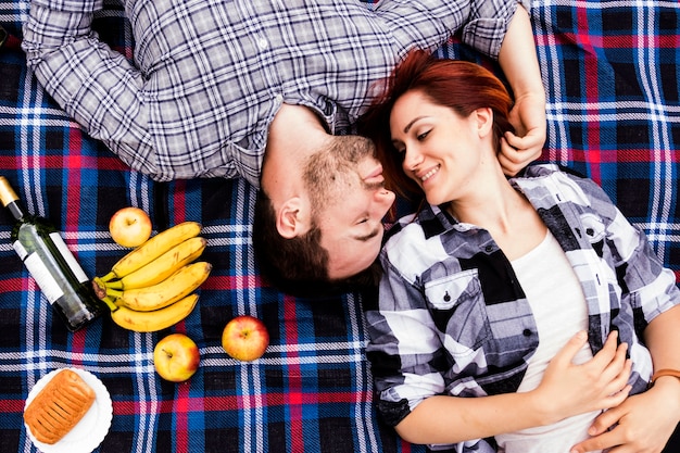 Liebevolle Frau mit ihrem Ehemann, der auf Decke mit vielen Früchten liegt