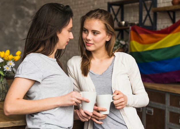 Liebevolle junge lesbische Paare, die die Tasse Kaffeetasse einander betrachtend halten