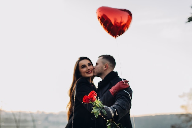 Liebevolle junge Leute mit Rosen und Ballon