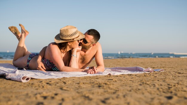 Liebevolle junge Paare, die sich zusammen entspannen und auf Sand am Sommerstrand liegen