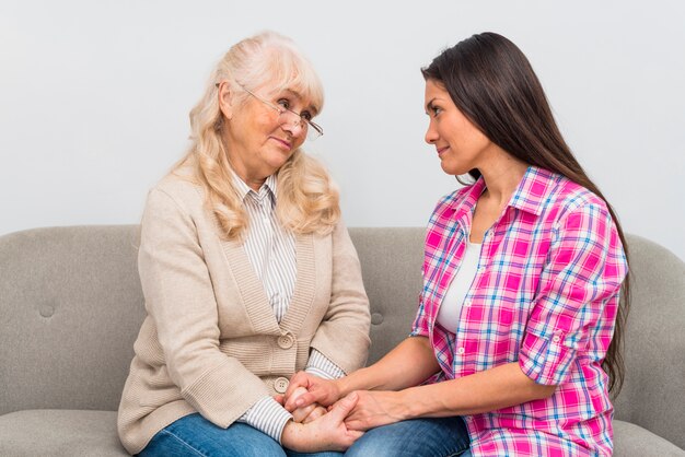 Liebevolle Mutter und Tochter, die einander Händchenhalten betrachtet, die auf Sofa sitzen