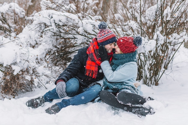 Kostenloses Foto liebevolle paare der umarmung, die auf schnee sitzen