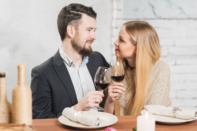 Liebevolle Paare, die mit Gläsern auf Abendessen klirren