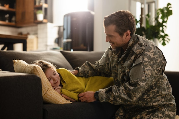 Liebevoller Soldat, der seine schläfrige Tochter anschaut, die zu Hause auf dem Sofa liegt