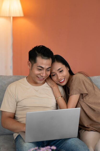 Liebevolles Paar zu Hause, das am Laptop arbeitet, während es auf dem Sofa sitzt
