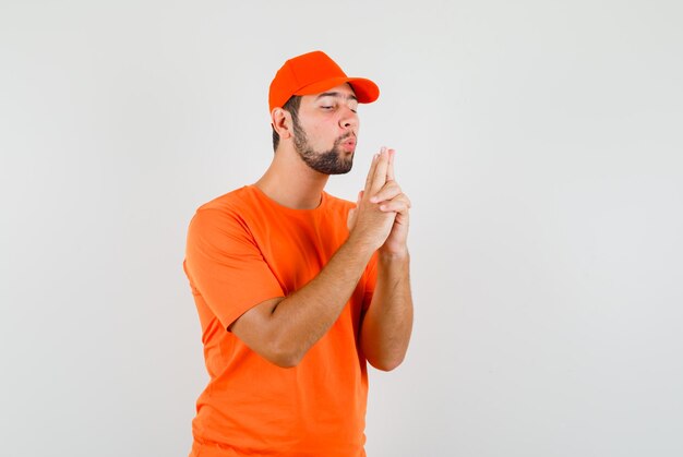 Lieferbote bläst auf Pistole, die von seinen Händen in orangefarbenem T-Shirt, Mütze, Vorderansicht gemacht wurde.