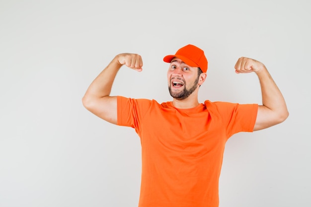 Lieferbote, der Arme in orangefarbenem T-Shirt, Mütze zeigt und mächtig aussieht. Vorderansicht.