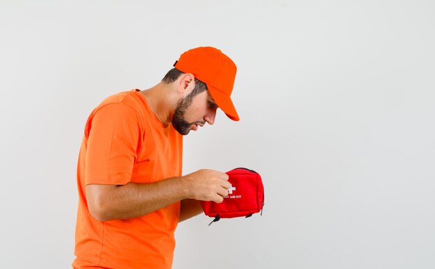 Lieferbote, der aufmerksam in Erste-Hilfe-Ausrüstung in orangefarbenem T-Shirt, Mütze schaut.
