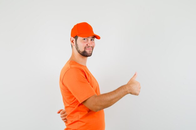 Lieferbote, der Daumen in orangefarbenem T-Shirt, Mütze zeigt und fröhlich aussieht. Vorderansicht.