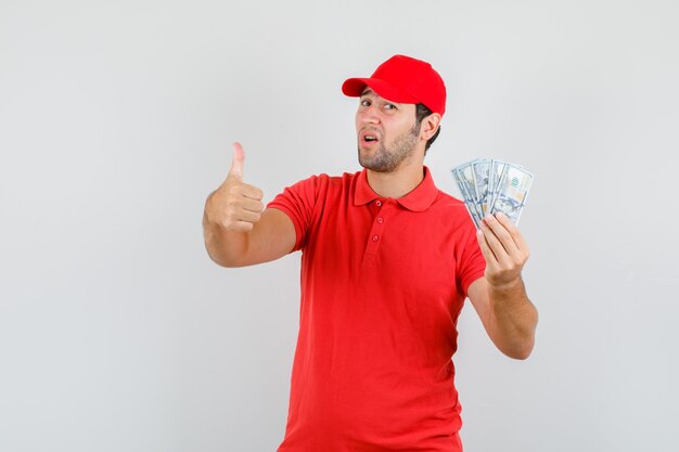 Lieferbote, der Dollarbanknoten mit Daumen oben im roten T-Shirt hält