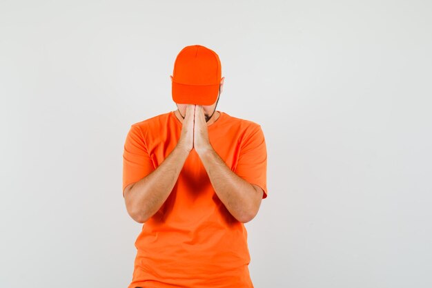 Lieferbote im orangefarbenen T-Shirt, Mütze, die Hände in betender Geste hält und ruhig aussieht, Vorderansicht.