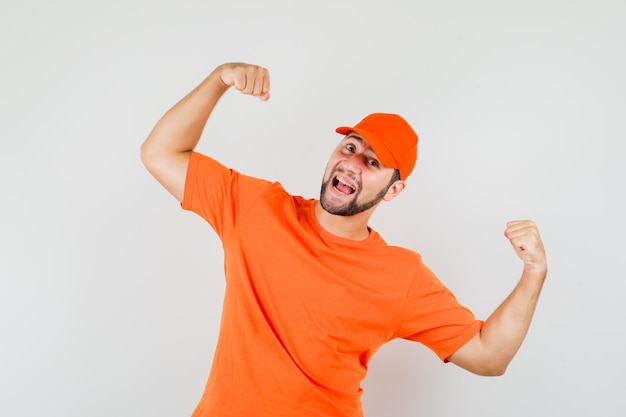 Lieferbote im orangefarbenen T-Shirt, Mütze mit Gewinnergeste und glücklichem Blick, Vorderansicht.