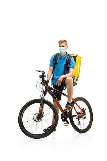 Kostenloses Foto lieferbote in gesichtsmaske mit fahrrad isoliert auf weißem studiohintergrund. kontaktloser service während der quarantäne. mann liefert essen während der isolation. sicherheit. beruflicher beruf. exemplar für anzeige.