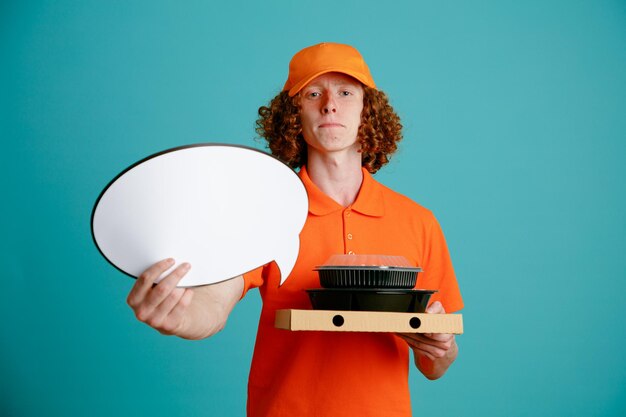 Lieferbote-Mitarbeiter in orangefarbener T-Shirt-Uniform mit leerer Sprechblase und Lebensmittelbehältern, die mit selbstbewusstem Ausdruck auf blauem Hintergrund in die Kamera blicken