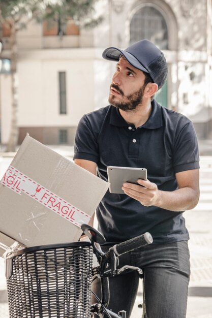 Lieferer, der auf Fahrrad mit digitaler Tablette und Paket sitzt