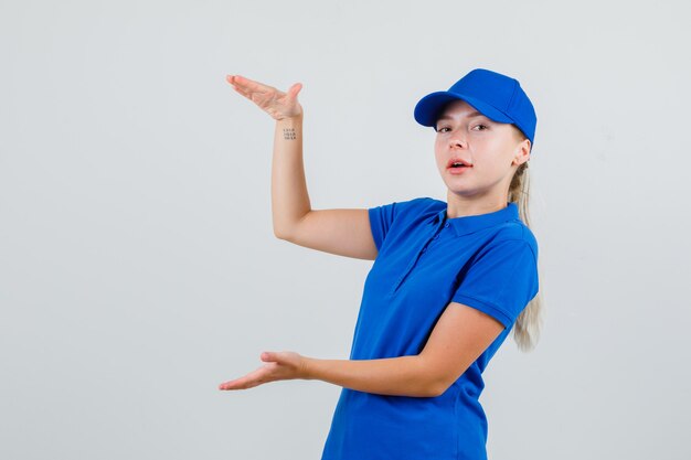 Lieferfrau, die Größenzeichen im blauen T-Shirt und in der Kappe zeigt und zuversichtlich schaut