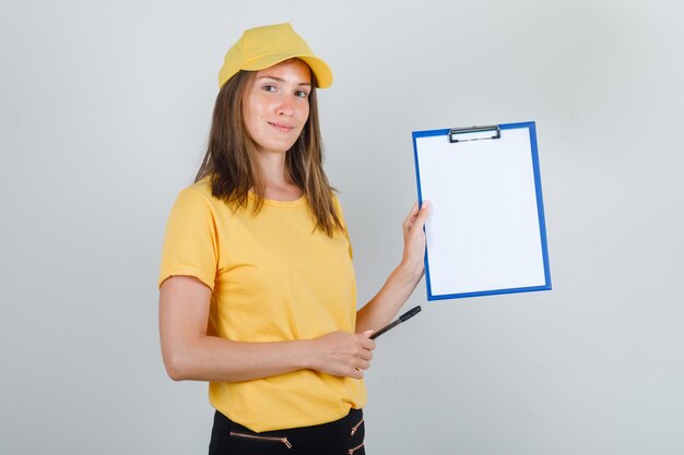 Lieferfrau, die Klemmbrett und Stift in T-Shirt, Hose, Mütze hält und fröhlich aussieht