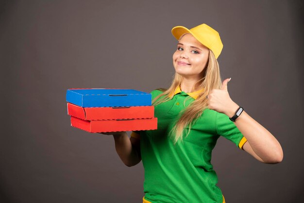 Lieferfrau, die Pappkartons der Pizza hält und Daumen oben zeigt. Hochwertiges Foto