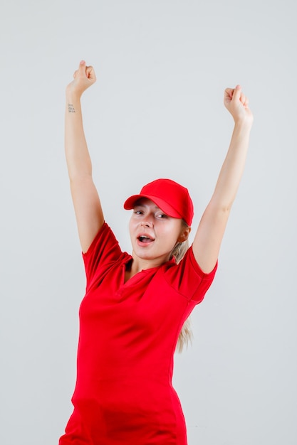 Lieferfrau, die Siegergeste im roten T-Shirt und in der Kappe zeigt und glücklich schaut