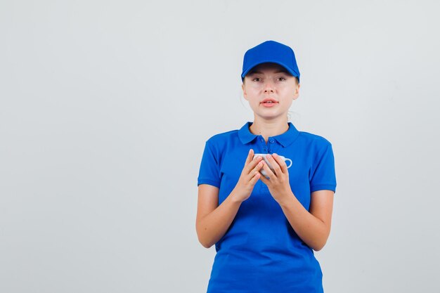 Lieferfrau im blauen T-Shirt und in der Kappe, die Tasse des Getränks halten