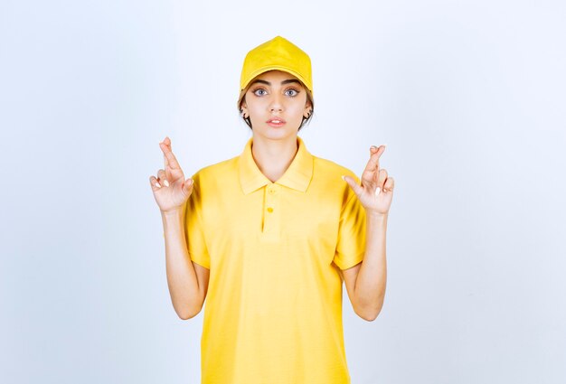 Lieferfrau in der gelben Uniform, die steht und gekreuzte Finger zeigt.