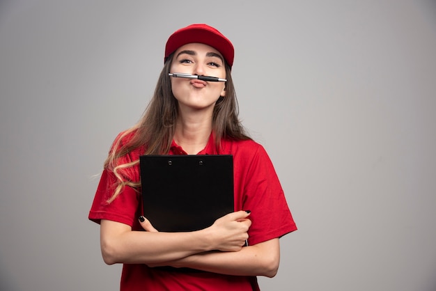 Kostenloses Foto lieferfrau in der roten uniform, die klemmbrett und stift hält.