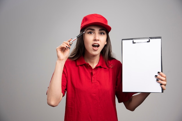 Lieferfrau in der roten Uniform, die Zwischenablage hält und spricht.