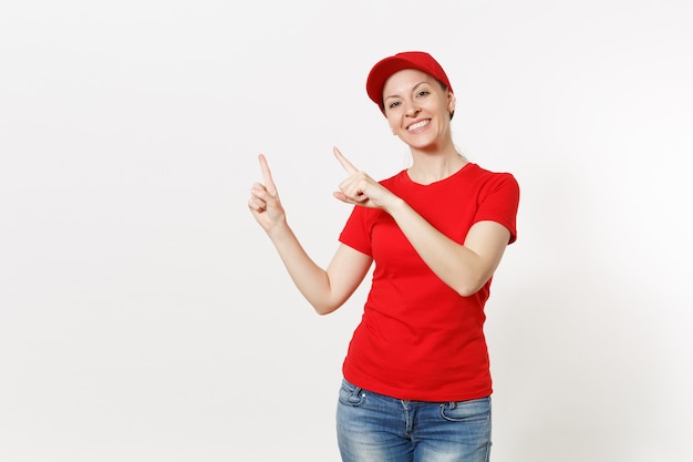 Lieferfrau in der roten uniform lokalisiert auf weißem hintergrund. professionelle kaukasische frau in mütze, t-shirt, jeans, die als kurier oder händler arbeitet und zeigefinger beiseite auf kopienraumwerbung zeigt.